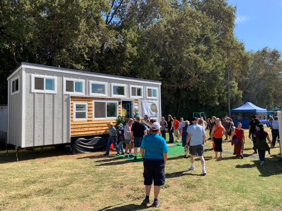 Completed white tiny home on wheels displayed at an outdoor event