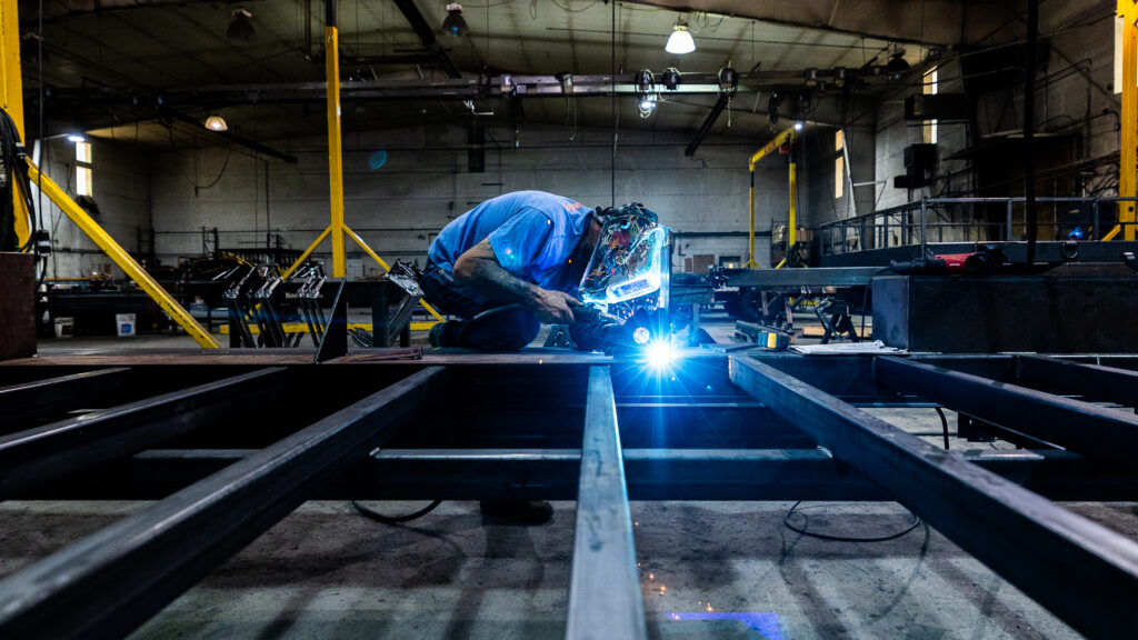 Welder fabricating a steel tiny house trailer frame in the Colorado factory