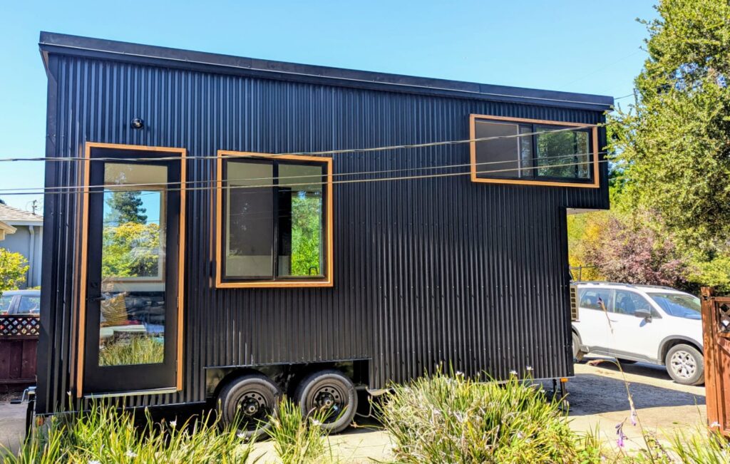 Black tiny home on wheels with wood-trimmed windows